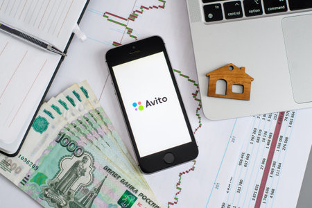 Vladimir, Russia - January 2022: A smartphone with the Avito application next to the figurine of the house. The concept of a service for finding a house to buy or sell. View from aboveのeditorial素材