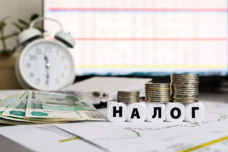 The inscription tax on white cubes against the background of an alarm clock and a monitor with...