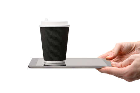 A paper cup for coffee stands on a digital tablet in hands on a white background. The concept of online ordering and food delivery. isolated object. Selective focus on the cup.の写真素材