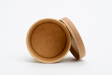 A round container with a lid for soup or ice cream lies on a white background. Eco-friendly food delivery container. Selective focus on leadの写真素材