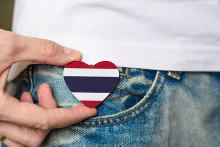 A resident of Thailand. Wooden badge with Thailand flag in the shape of a heart in a man's hand.の写真素材