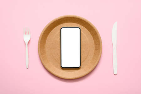 A smartphone with a blank white display lies on a paper empty plate on a pink background. Food delivery service advertising concept.の写真素材