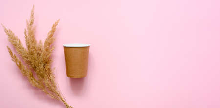 A brown paper cup for coffee and a dry bouquet of grass on a pink background. copyspace. The concept of using eco-friendly disposable tableware to protect nature.の写真素材