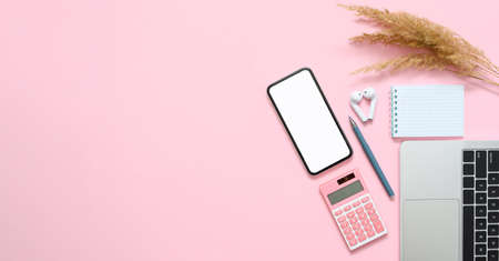 Women's workplace in the office. Smartphone with a blank white display, laptop, notepad and a bunch...