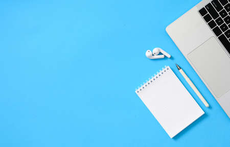 Notepad with a pen next to a laptop on a blue background. diagonal arrangement. Notepad with blank white sheet. To the left is an empty space. view from above.の写真素材