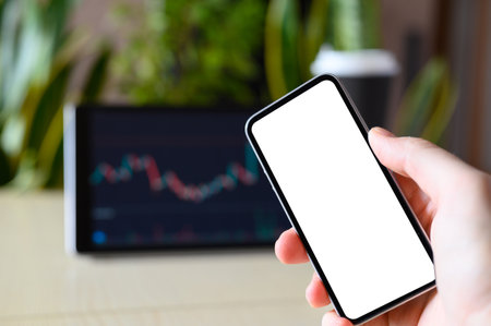 Smartphone with a blank white display in hand on the background of a tablet with charts and plants. Workplace in the office. selective focus. Template for advertising.の写真素材