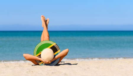 A slender girl on the beach in a straw hat in the colors of the Tanzania flag. The concept of a perfect vacation in a resort in the Tanzania and Zanzibar. Focus on the hat.の写真素材