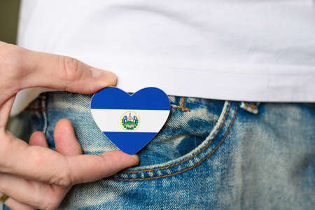 Wooden badge with El Salvador flag in the shape of a heart in a man's hand.の写真素材