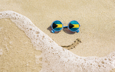 Sunglasses with flag of Bahamas on a sandy beach. Nearby is a sea lightning and a painted smile. The concept of a successful vacation in the resorts of Bahamas.の写真素材