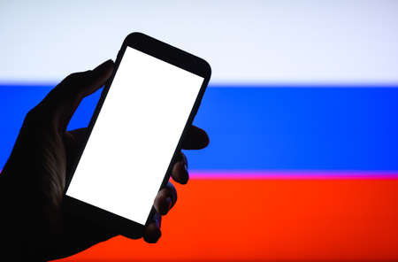 Smartphone with a white blank display in hand against the background of the Russian flag. Mock up.