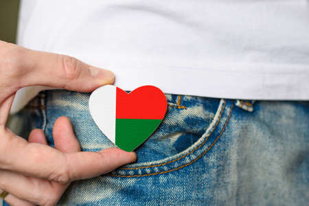 Tourist or resident of Madagascar. Wooden badge with Madagascar flag in the shape of a heart in a man's hand.の写真素材