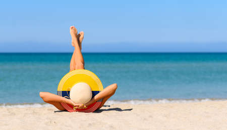 A slender girl on the beach in a straw hat in the colors of the Colombian flag. The concept of a perfect vacation in a resort in the Colombia. Focus on the hat.の写真素材