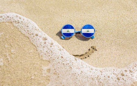 Sunglasses with flag of Nicaragua on a sandy beach. Nearby is a sea lightning and a painted smile. The concept of a successful vacation in the resorts of Nicaragua.の写真素材