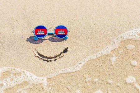 A painted smile on the sand and sunglasses with the flag of the Cambodia. The concept of a positive and successful holiday in the resort of Cambodia.の写真素材