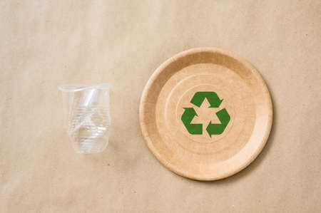 A paper eco-friendly plate with a recycling green sign next to a plastic disposable cup. The concept of using biodegradable tableware.の写真素材