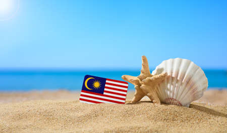 Tropical beach with seashells and Malaysian flag. The concept of a paradise vacation on the beaches of Malaysia.の写真素材