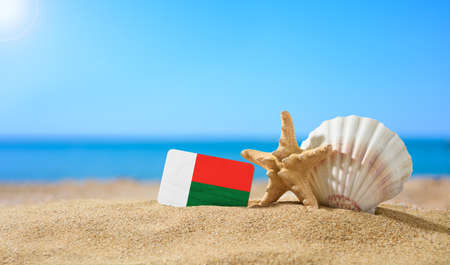 Tropical beach with seashells and Madagascar flag. The concept of a paradise vacation on the beaches of Madagascar.の写真素材