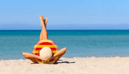 A slender tanned girl on the beach in a straw hat in the colors of the flag of Catalonia. Focus on the hat.の写真素材
