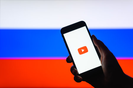 Vladimir, Russia - April 2022: Starting the YouTube app on a smartphone against the background of the Russian flag. Selective focus on logoのeditorial素材
