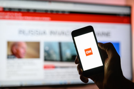 Vladimir, Russia - February 2022: A smartphone with an application for viewing CNN world news in hand against the background of the open CNN website. Selective focus on the logo.のeditorial素材