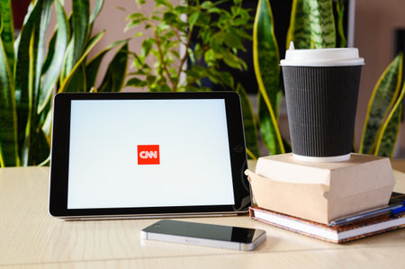 Vladimir, Russia - February 2022: Watching the news during your lunch break. The CNN app on a tablet for watching world news. Selective focus on the logo.のeditorial素材