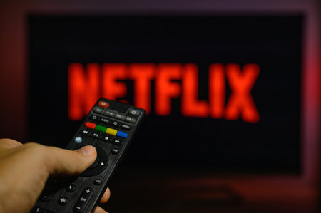 Vladimir, Russia - November 2021: hand with a black remote control on the background of a TV with a Netflix screensaver. Selective focus on the hand with the remote control.のeditorial素材