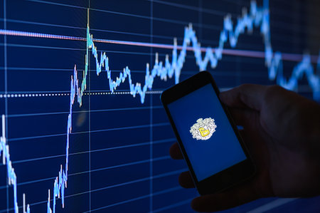 Vladimir, Russia - January 2022: Tinkoff app on a smartphone against the background of charts in the dark. Selective focus on the logo.のeditorial素材