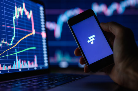 Vladimir, Russia - January 2022: FTX cryptocurrency trading application on a smartphone in hand against the background of monitors with financial charts. Selective focus on the logo.のeditorial素材