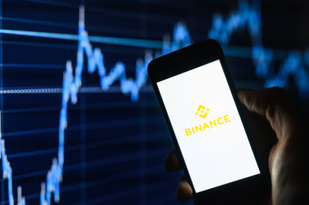 Vladimir, Russia - January 2022: Benance cryptocurrency trading app on a smartphone against the background of charts in the dark. Selective focus on the logo.のeditorial素材