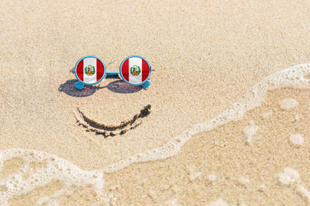 A painted smile on the sand and sunglasses with the flag of Peru. The concept of a positive and successful holiday in the resort of Peru.の写真素材