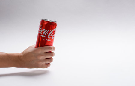 Vladimir, Russia - November 2021: A can of Coca-Cola in a female hand on a light background. On the right is an empty free space.のeditorial素材
