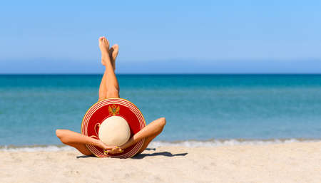 A slender girl on the beach in a straw hat in the colors of the flag of Montenegro. The concept of a perfect vacation in a resort in the Montenegro. Focus on the hat.の写真素材