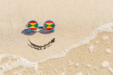 Sunglasses with flag of Grenada State on a sandy beach. Nearby is a sea lightning and a painted smile. The concept of a successful vacation in the resorts of Grenada.の写真素材