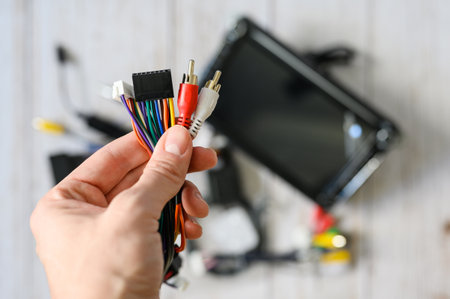 A bundle of wires with various connectors in hand against the background of a new car radio. Selective focus on hand with wiresの写真素材