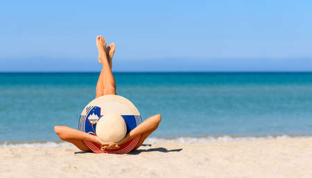 A slender girl on the beach in a straw hat in the colors of the flag of Slovenia. The concept of a perfect vacation in a resort in the Slovenia. Focus on the hat.の写真素材