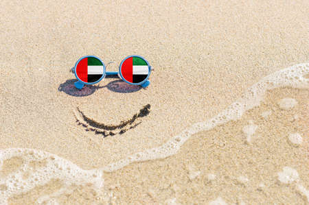 A painted smile on the beach and sunglasses with the flag of the United Arab Emirates. The concept of a positive and successful holiday in the resort of the United Arab Emirates.の写真素材