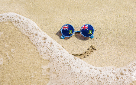 Sunglasses with flag of British Virgin Islands on a sandy beach. Nearby is a sea lightning and a painted smile. The concept of a successful vacation in the resorts of the British Virgin Islands.の写真素材