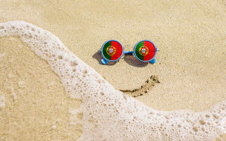 Sunglasses with flag of Portugal on a sandy beach. Nearby is a sea lightning and a painted smile. The concept of a successful vacation in the resorts of the Portugal.の写真素材
