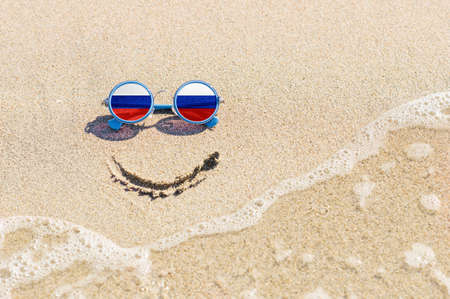 A painted smile on the beach and sunglasses with the flag of the Russia. The concept of a positive holiday in the resort of the Russia.の写真素材