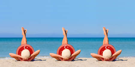 Three young girls on the beach wearing straw hats in the colors of the flag of Turkey. The concept of the perfect holiday in the resorts of the Turkey. Focus on hats.の写真素材
