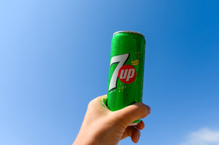 Anapa - Russia, July 2022: Cold can of 7 up soft drink in hand against blue sky. Selective focus on...