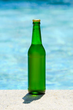 A bottle of cold beer stands by the pool on a hot summer day. vertical format.の写真素材