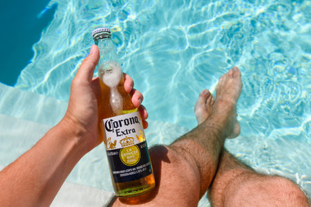 Novorossiysk - Russia, July 2022: A bottle of cold beer in a man's hand by the pool on a hot summer day. Beer Corona Extraのeditorial素材