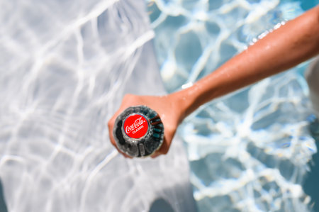 Novorossiysk - Russia, July 2022: A bottle of Coca Cola in the girl's hand in the hotel pool....