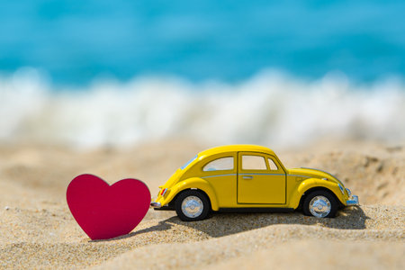 Anapa - Russia, July 2022: Toy yellow car and wooden heart on the sandy seashore. The concept of auto travel loversのeditorial素材