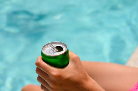 Close-up of an open can of a drink in a hand against the backdrop of a swimming pool. Selective focus on a hand with a drink.の写真素材