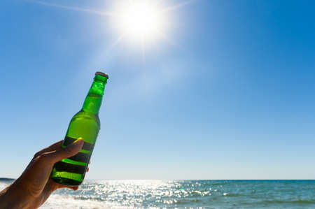 a bottle of cold beer in a hand against the backdrop of the bright rays of the sun. The concept of a good beach holidayの写真素材