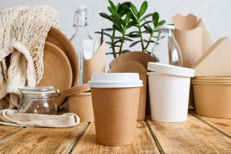 Close-up of a paper disposable cup against the background of a set of eco-friendly tableware and a green plant. Zero waste concept. Selective focus on cupの写真素材