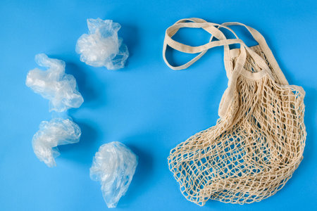 Several plastic bags opposite one eco-friendly shopping bag on a blue background. The concept of replacing plastic with environmentally friendly materials. Flat lay, copy space.の写真素材
