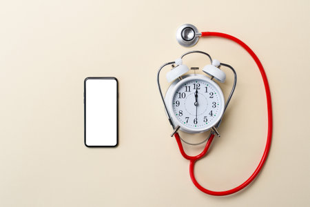 Smartphone with a blank white display next to an alarm clock and a stethoscope. Advertisement for medical diagnostic centers.の写真素材